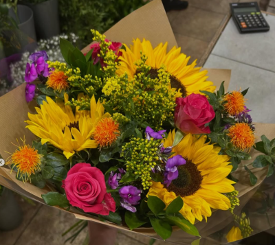 Vibrant Sunflower Bouquet - A lively and expressive bouquet bursting with warm, radiant tones and playful pops of color. This arrangement blends bold golden hues with vibrant pinks, oranges, and purples, creating a joyful, energetic feel. Full of texture and movement, it’s wrapped in natural kraft paper for a relaxed yet polished finish—perfect for celebrating special moments or adding a cheerful glow to any space.